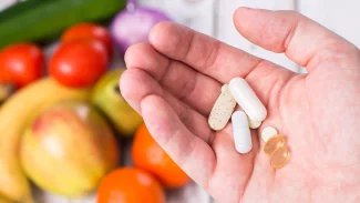 Ruka drží tablety a tobolky nad stolem s s ovocem a zeleninou