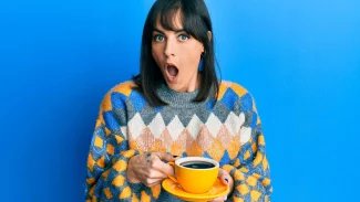 Mladá žena s vyděšeným výrazem stojí s hrnkem s kávou v ruce