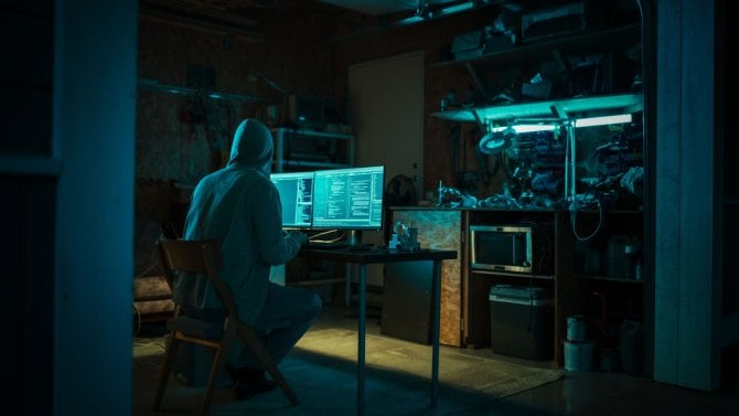 Domácí garáž pozdě v noci: Zlovolný hacker v mikině s kapucí se vloupá do datových serverů, DDOS útok, phishingový útok, malware. Muž píše kód pro trojského koně. Koncept kyberkriminality na darknetu.
