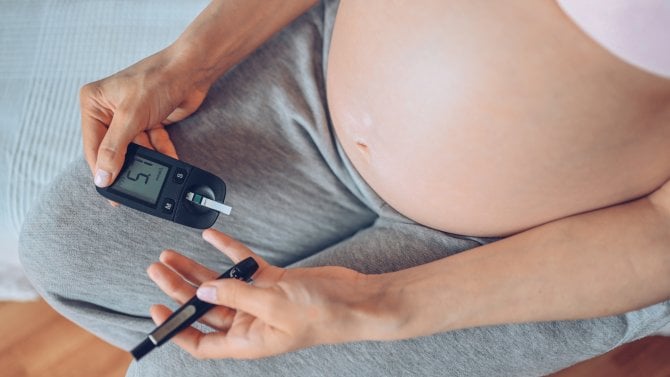 Detail břicha těhotné ženy, která používá glukometr