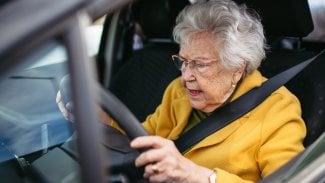 Seniorka sedí ve voze za volantem a tváří se trochu zoufale