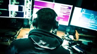 hacker s kapucí před třemi monitory