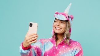 Mladá šťastná žena v kostýmu jednorožce s telefonem v ruce
