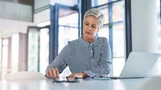 Starší hezká žena u počítače v kanceláři počítá na kalkulačce