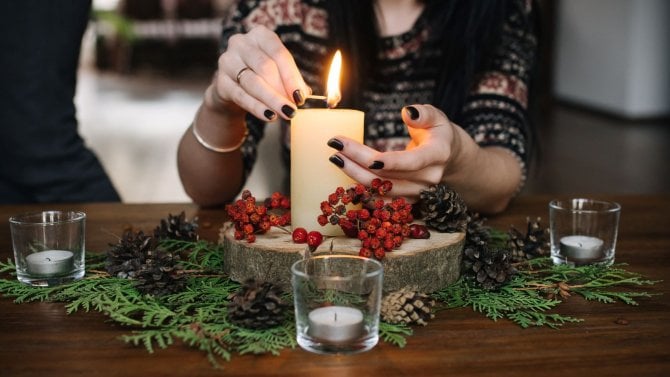Žena zapaluje svíčku na vánoční výzdobě