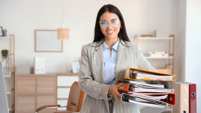 Mladá úřednice v kanceláři držící několik šanonů s dokumenty