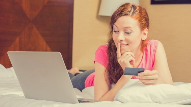 Mladá žena leží v posteli a zvažuje nákup na internetu