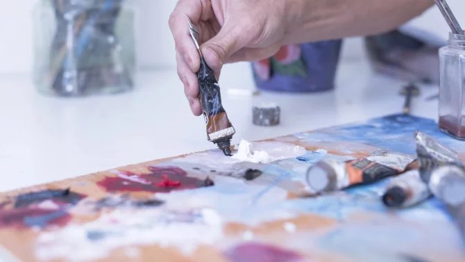 Malířský ateliér, detailní záběr na ruku a tubu s barvou
