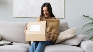 Žena na gauči nadšeně rozbaluje objednaný balíček