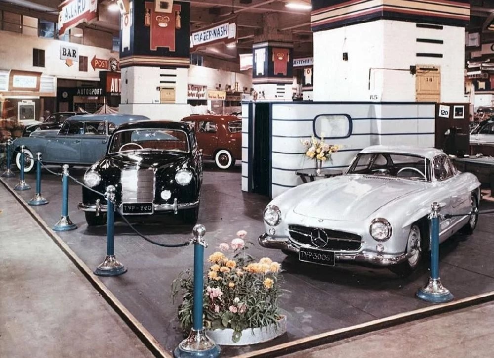 Na stánku Mercedes-Benz v londýnském Earls Courtu je mezi bílým supersportem 300 SL a modrým W186 „Adenauer“ elegantní černý 220