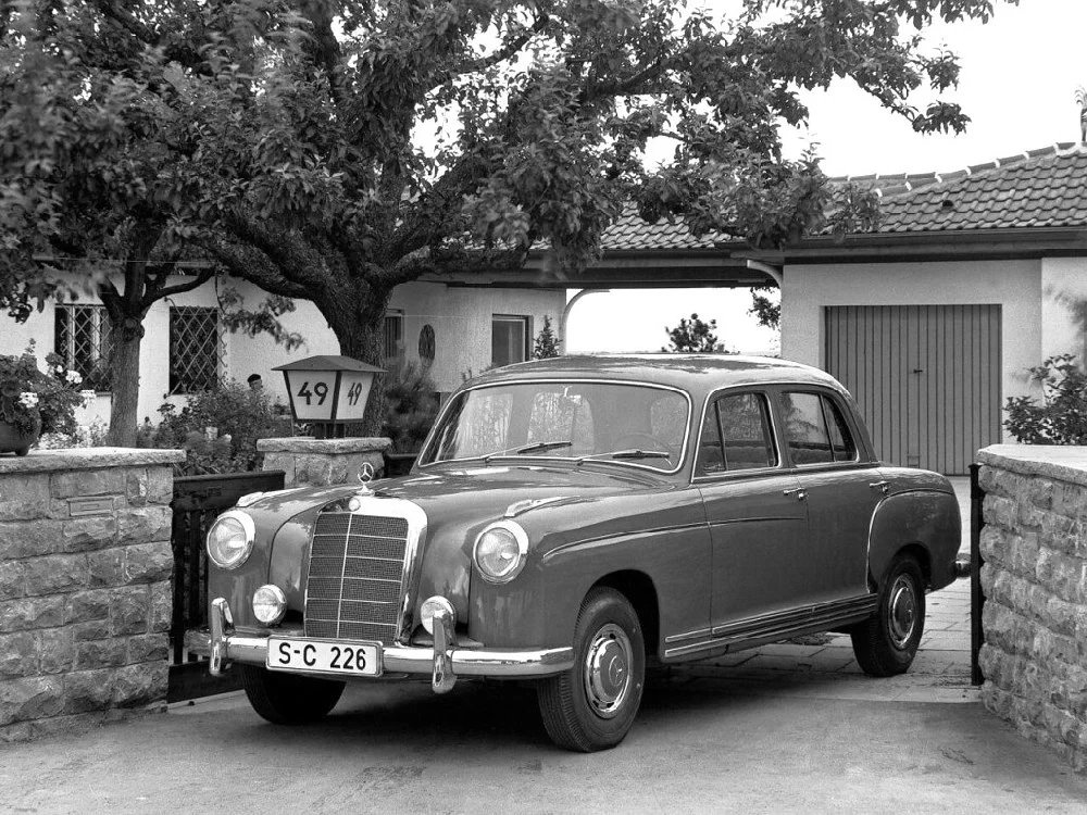 Německý sen, zhmotněný do propagační fotografie: Mercedes-Benz 220 na vjezdové cestě před garážovými vraty u novostavby v předměstském stylu padesátých let
