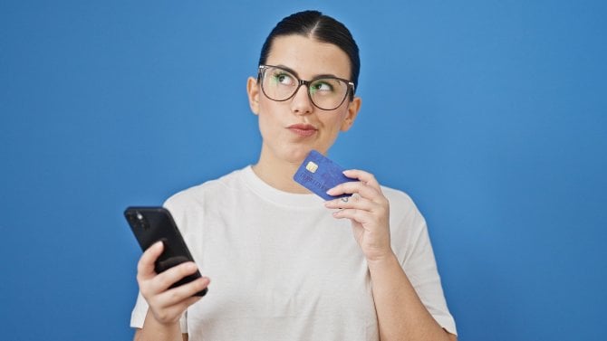 Žena váhá, zda platit mobilem nebo kartou