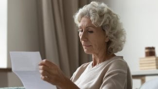 Důchodkyně si čte dopis na sedačce