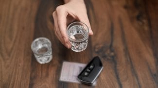 Detail ruky se skleničkou, klíčů od vozu a řidičského průkazu na stole