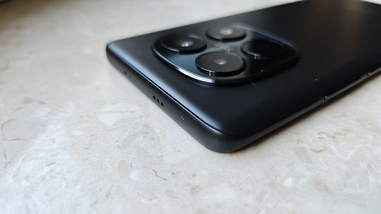 Černý Redmi Note 15 položený na světlé podložce, detail horní hrany a zadních fotoaparátů.