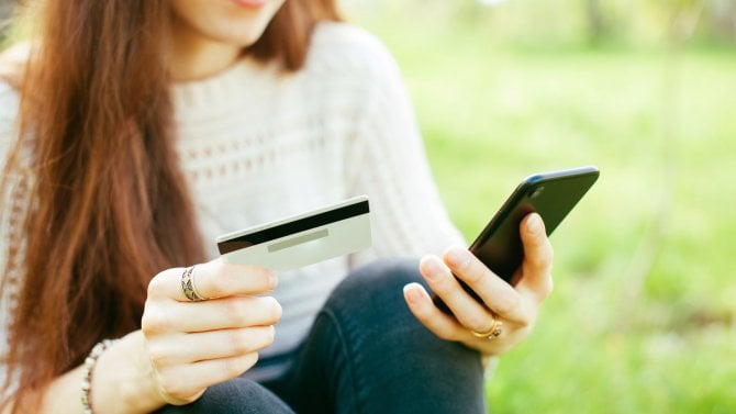 Mobilní platby. Ženské ruce (zaostřené) používající smartphone a (rozmazanou) kreditní kartu s notebookem pro online nakupování, mobilní bankovnictví.