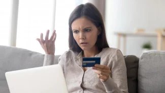 Žena  s rozlobeným výrazem sedí u počítače, v jedné ruce drží platební kartu