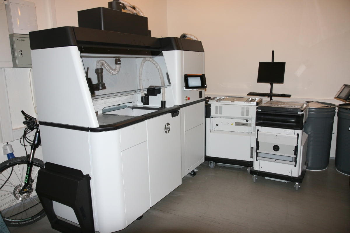 Další jednotka, která je větší než samotná tiskárna, slouží k čištění a odsání přebytečného prášku, ten je následně recyklován do dalšího tisku.