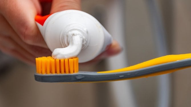 Zubní pasta nanesená na oranžovošedém zubním kartáčku