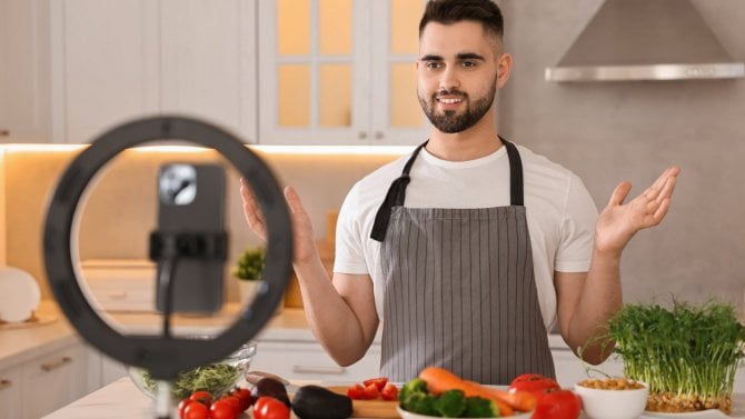 Foodbloger vaří při nahrávání videa s chytrým telefonem a kruhovou lampou v kuchyni