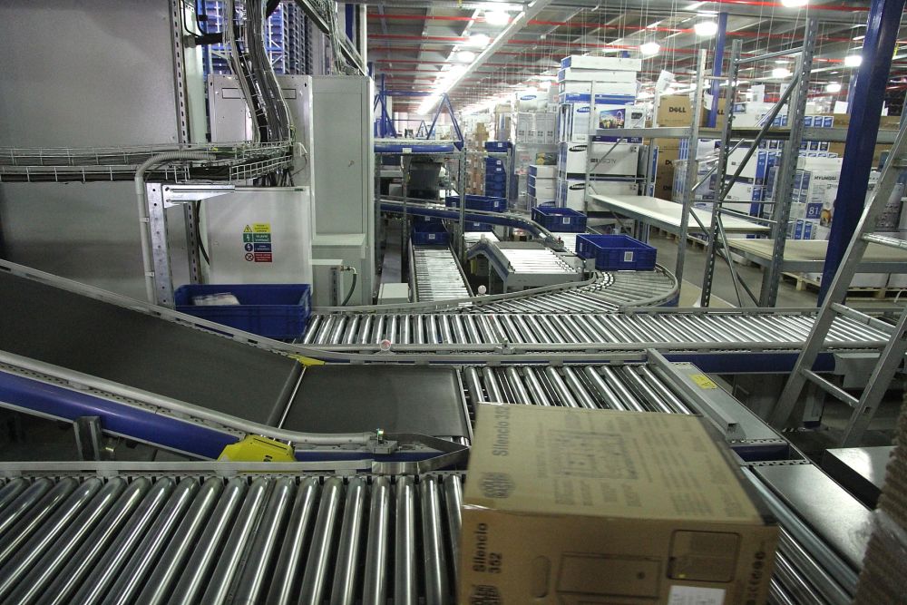 Práci usnadňuje sofistikovaný logistický systém. V hale jsou zhruba dva kilometry dopravníkových (většinou válečkových) tratí. Zboží se na nich pohybuje rychlostí až 0,9 m/s. Co chvíli kolem vás prodeje krabice či modrá přepravka.