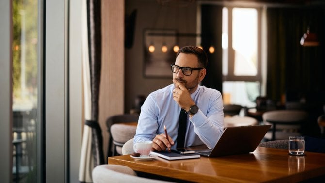 Zamyšlený podnikatel sedící u stolu před notebookem