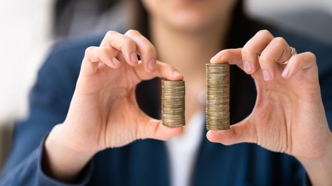 Žena držící dva různě vysoké sloupky mincí.