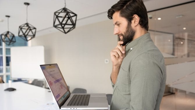 Muž v kanceláři drží telefon a nad něčím se zamýšlí