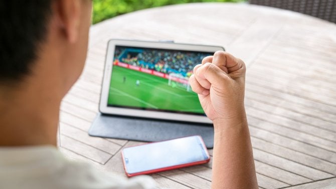 Muž se vztyčenou pěstí při sledování fotbalového zápasu na digitálním tabletu. Živý přenos nebo sportovní online koncept.