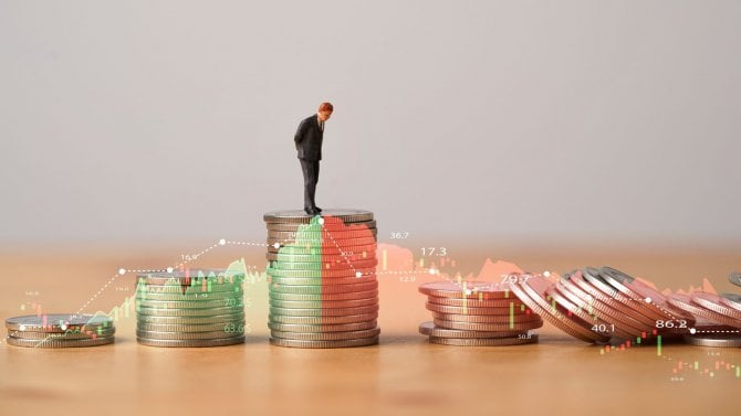 Hromádky minci, které rostou a nejvyšší hromádce stojí muž v obleku. Následně hromádky klesají