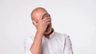 Zoufalý plešatý starší muž si drží obličej v dlani