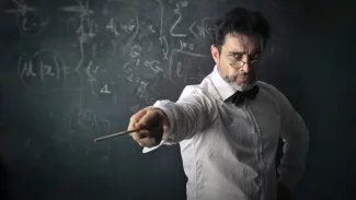 Přísný učitel s ukazovátkem před tabulí.