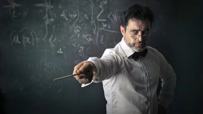 Přísný učitel s ukazovátkem před tabulí.