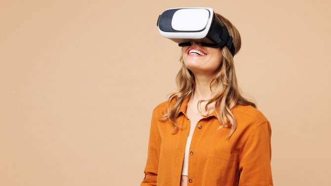 Mladá usměvavá šťastná veselá žena nosí oranžové tričko ležérní oblečení sledující ve VR headsetu pc gadget. Koncept životního stylu