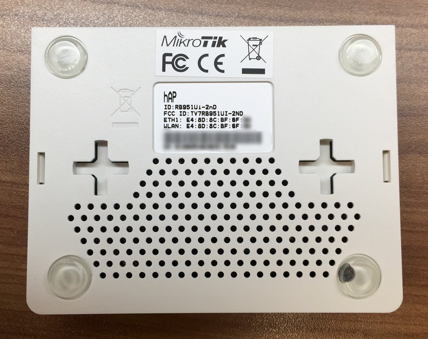 Spodní strana routeru MikroTik hAP s řadami větracích otvorů a čtyřmi nožkami.