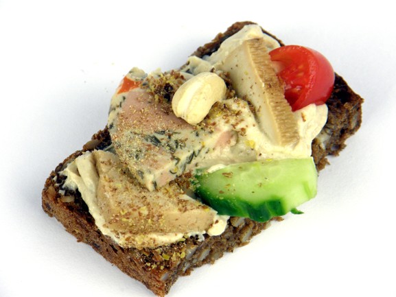 Česneková pochoutka - Celozrnný žitný chléb s chia semínky lehce namažeme česnekovou rostlinnou pomazánkou, na to položíme uzené tofu, vaječný nářez s mořskou řasou, přidáme kešu oříšek, ozdobíme okurkou a cherry rajčátkem a posypeme nadrceným lněným semínkem.
