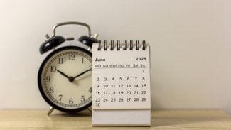Na stole je budík a měsíční kalendář s měsícem červnem 2025