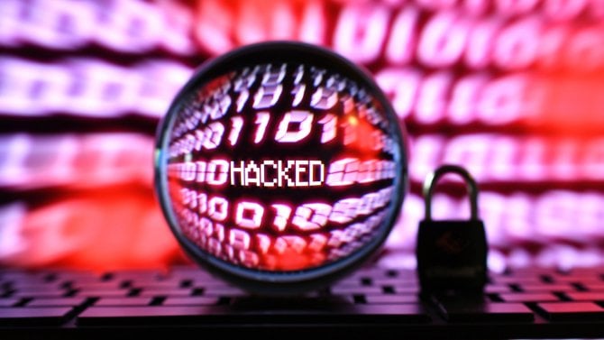 Červená obrazovka s binárním kódem počítače a nápisem „hacked“ viditelná přes čočku s visacím zámkem na klávesnici. Koncept pro kybernetický útok hackera, podvod, podvod.