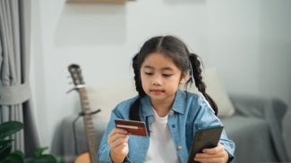 Holčička s copy držící v ruce platební kartu a mobilní telefon.