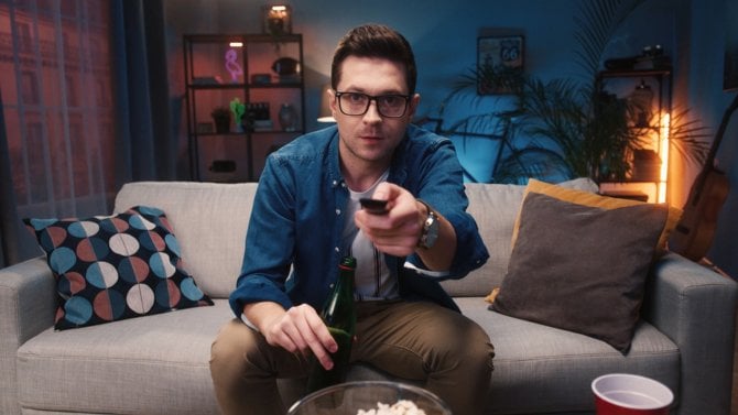 Muž sledující na gauči televizi s ovladačem v ruce