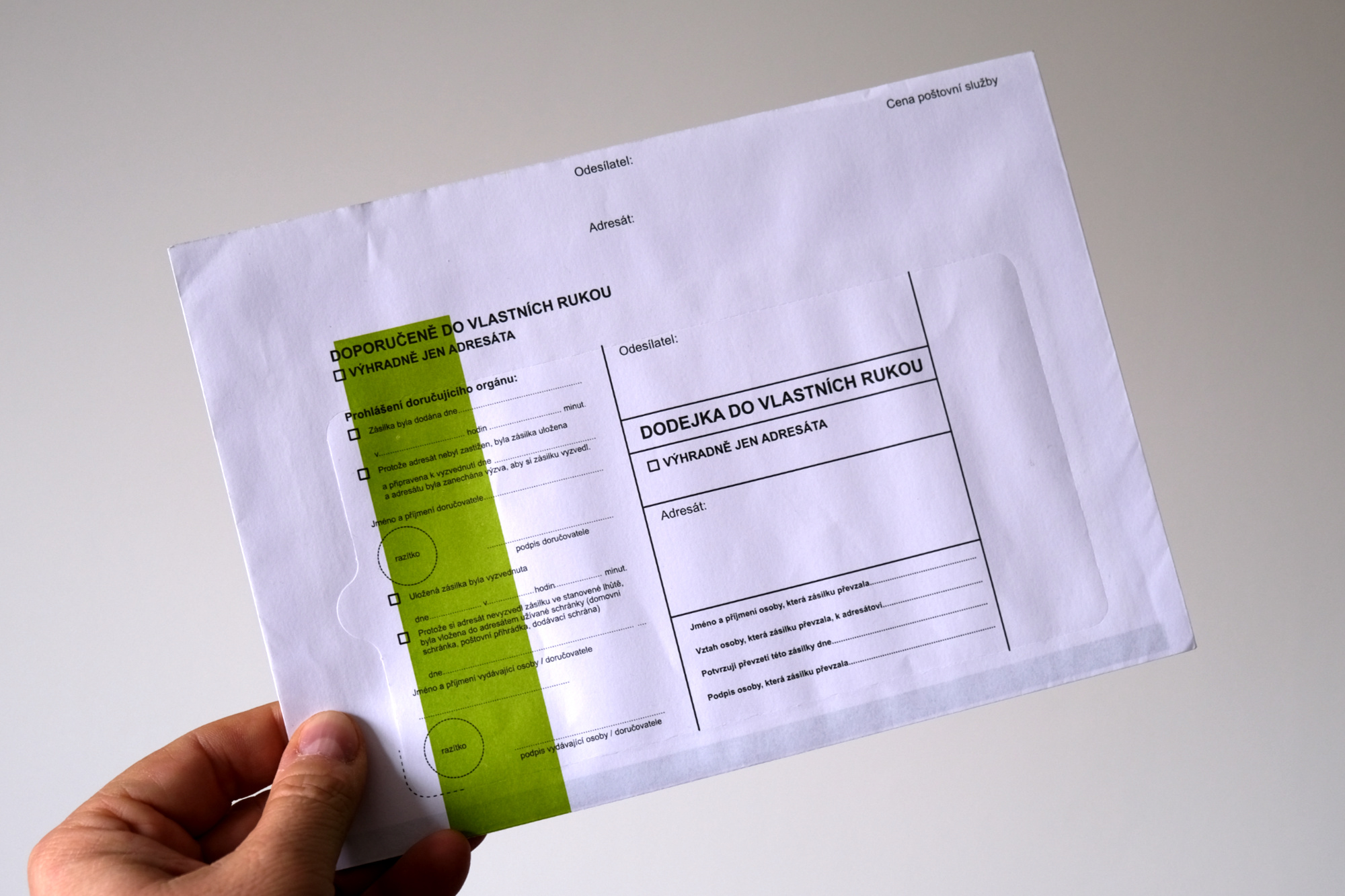 Ruka držící obálku se zeleným pruhem.