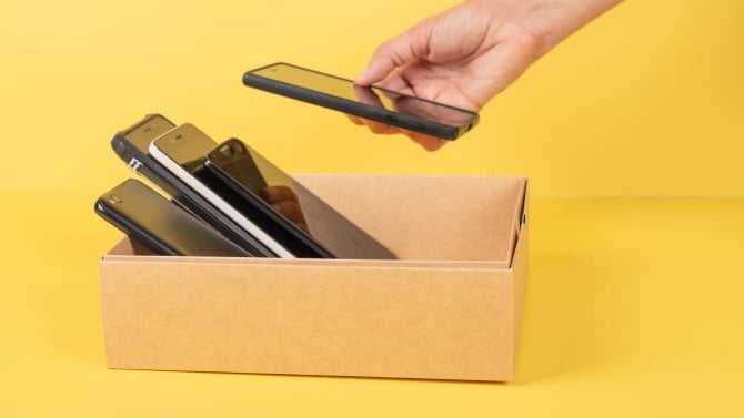 Darování použitých mobilních telefonů. Vložte starý mobilní telefon do kartonové krabice plné použitých smartphonů. Darování, elektronický odpad, charita zaměřená na elektronický odpad, koncept recyklace