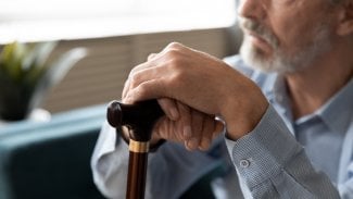 Muž ve středním věku sedí opřený o berle a je zamyšlený