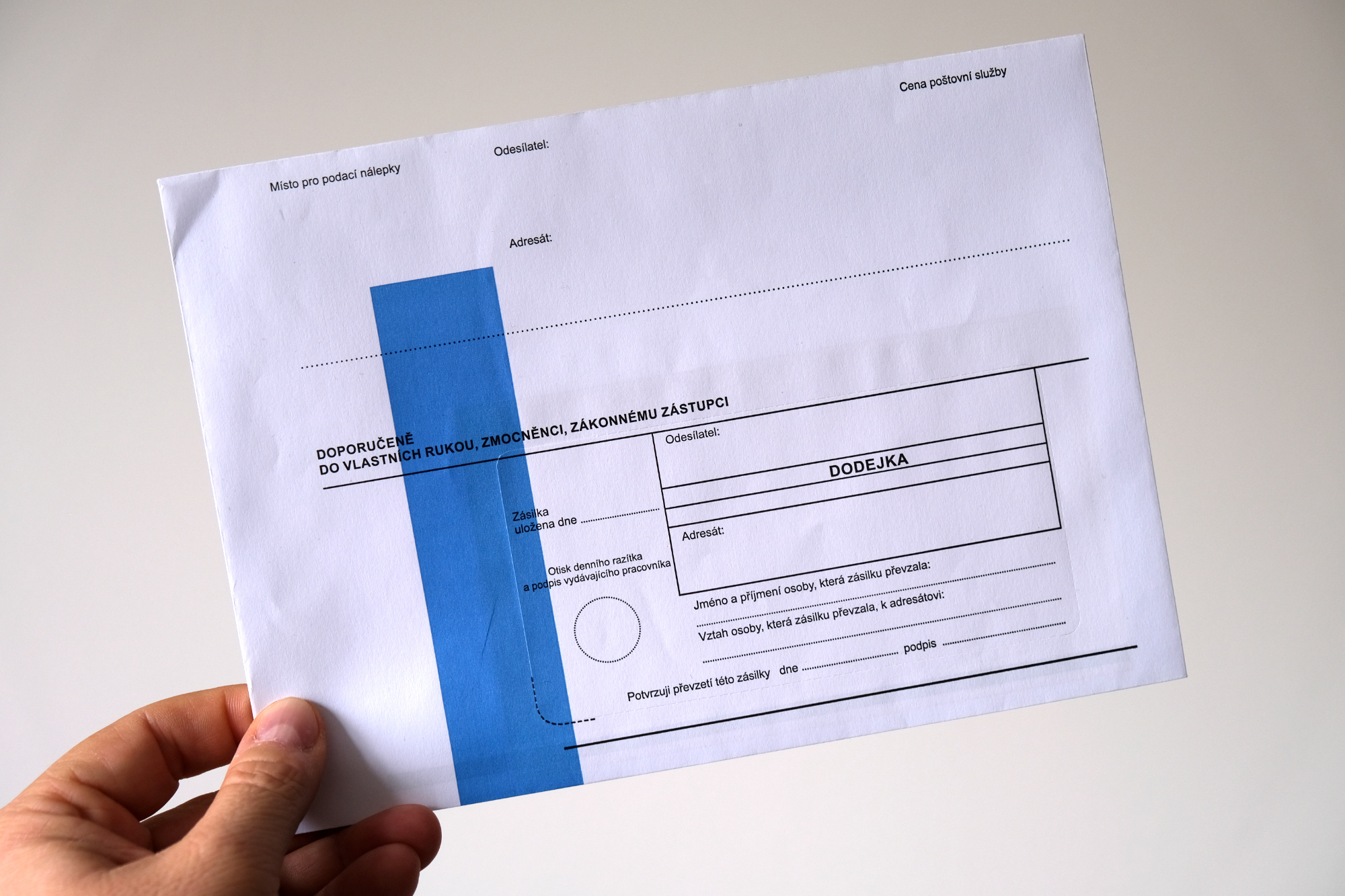 Ruka držící obálku s modrým pruhem.