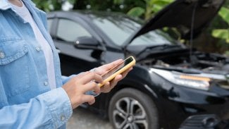 Žena stojící u rozbitého auta s telefonem v ruce.