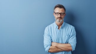 Starší muž, dobře vypadající penzista, stojí a vážně se tváří, ruce má založení