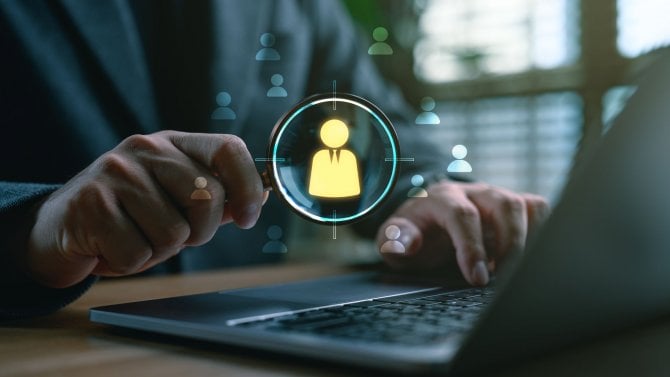 Muž v kanceláři s notebookem držící lupu se symbolem zaměstnance