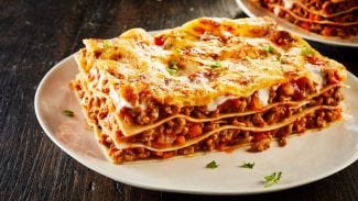 Lasagne s mletým masem na bílém talíři, zdobené čerstvou bazalkou
