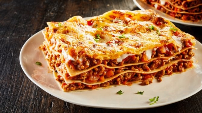 Lasagne s mletým masem na bílém talíři, zdobené čerstvou bazalkou