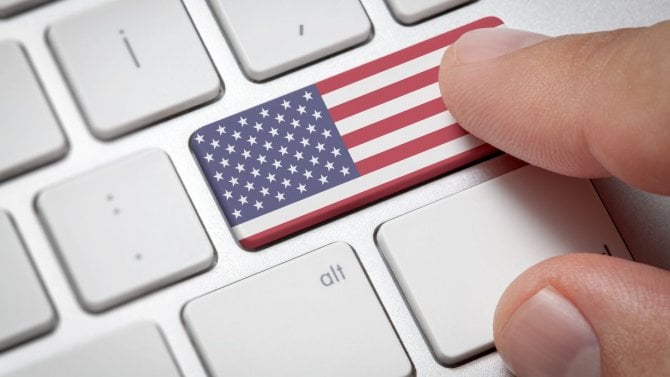 Online koncept mezinárodního obchodu: Počítačový klíč s vlajkou Spojených států amerických. Mužská ruka mačkající klávesu počítače s americkou vlajkou.